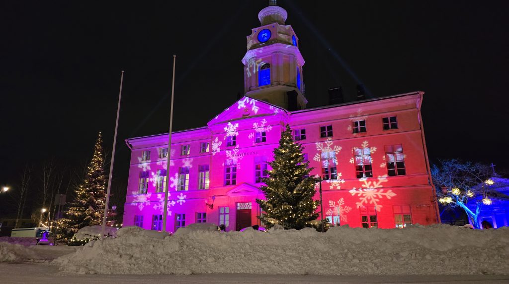 Valaistu Raatihuone lumivallin takana.